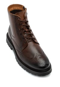 Brązowy skórzany botek za kostkę z detalami w stylu brogue, okrągłym noskiem i kontrastującą podeszwą. Posiada sznurówki, wyściółkę kołnierza i teksturowane wykończenie.