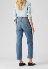 Jeans de mezclilla azul claro con corte recto, talle alto y un sutil bordado en los bolsillos traseros. Combinados con una camisa azul clara y flats negros.