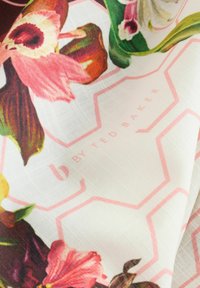 Auduma ar ziedu rakstu, kurā ir rozā un zaļi ziedi, kā arī gaiši rozā sešu stūru kontūras uz balta fona, marķēts ar "by Ted Baker".