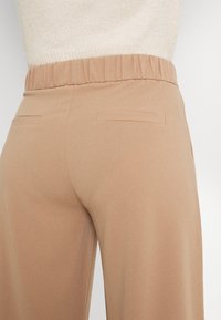 Beżowe spodnie typu wide-leg z elastycznym pasem, gładką teksturą i dwiema tylnymi kieszeniami. Idealne na co dzień.