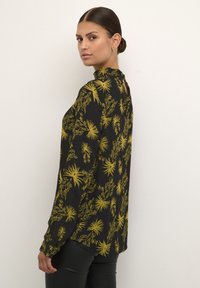 Blusa nera a maniche lunghe con stampa floreale gialla, dotata di colletto alto e leggera apertura sul retro. Texture morbida con vestibilità ampia.