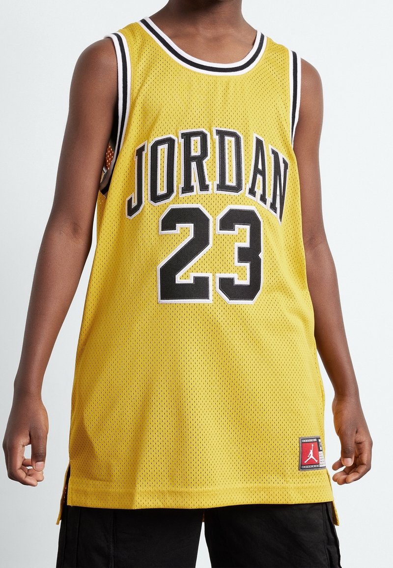 Żółta siatkowa koszulka do koszykówki z napisem "JORDAN" i numerem "23" w kolorze czarnym, z czerwoną metką logo na bocznym szwie i szczelinami po bokach dla lepszej wentylacji.