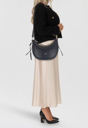 Navy Leder Schultertasche mit goldenen Beschlägen, glatter Textur und Reißverschluss. Tragen Sie sie mit einer schwarzen Jacke und einem beigen Satinrock.