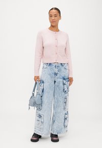 Jasnoróżowy dziergany kardigan z okrągłym dekoltem i zapięciem na guziki, w zestawie z oversize'owymi jasnoniebieskimi spodniami cargo z denimu z wieloma kieszeniami.
