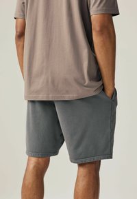 Graue Baumwollshorts mit einem lockeren Schnitt und Seitentaschen, kombiniert mit einem taubfarbenen Kurzarm-T-Shirt. Einfaches Design, lässiger Stil.