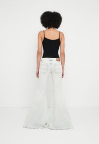 Valged luitunud teksapüksid kõrge vöökohaga, millel on viie taskuga disain, tuhmunud efekt ja tagatasku õmbluse detail. Must keha jälgiv topp.