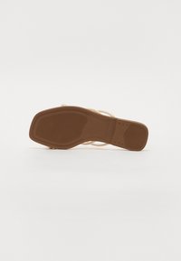 Beige remsandale med en struktureret brun sål, flad design og minimalistisk stil med tynde stropper over foden.