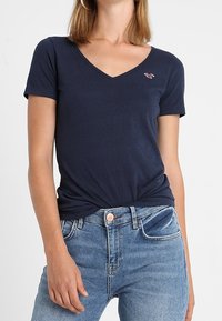 Námořnická modrá tričko s krátkým rukávem a V-výstřihem, slim fit s malým logem na levé straně hrudi. Měkká bavlněná tkanina s mírným strečem.