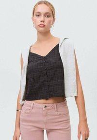 Svart rutigt kort topp med framknappar, lager under en ljusgrå tröja som hänger över axlarna, i kombination med rosa jeans.