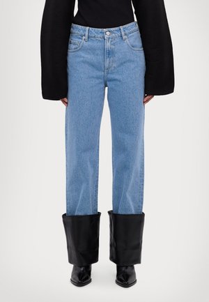 Light blue denim jeans with a straight-leg fit, featuring black leather flared cuffs and a button waistband. Black long-sleeve top visible.