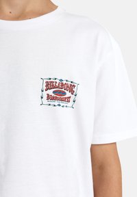T-shirt in cotone bianco con un logo colorato ricamato sul lato sinistro del petto, con la scritta "BILLABONG Boardshorts."