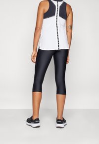 Vit ärmlös träningslinne med svarta accenter och logodetaljer, matchat med svarta cropped leggings. Texturerad tyg, figurnära design.