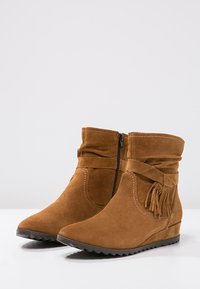 Bruine suède enkellaarsjes met een slouchy ontwerp, zijrits, franjes en een gestructureerde rubberen zool. De wigvormige hak verhoogt het comfort.