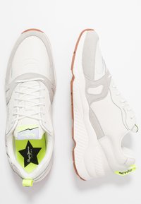 Białe i jasnoszare sneakersy z teksturowanej skóry i zamszu, z neonowymi żółtymi akcentami oraz gumową podeszwą o teksturowanym wzorze.