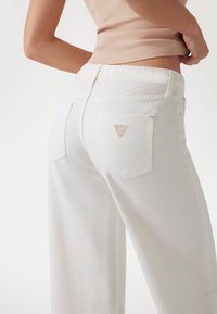 White wide-leg jeans made of cotton, featuring a high waist, back pockets, and a small logo detail in a triangle shape on the right pocket.
