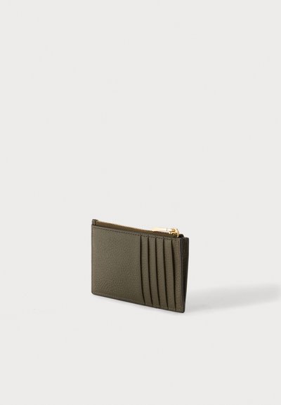 Porte-cartes en cuir vert foncé avec cinq emplacements verticaux pour cartes et une poche zippée dorée sur un fond gris clair.