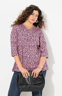 Roze blouse met een zwart dierenprintpatroon, v-hals, driekwartmouwen en een losse fit. Gedragen met donkere jeans en een zwarte tas.