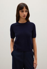 Maglione navy a maniche corte con collo rotondo, texture morbida e design aderente. Abbinato a pantaloni scuri; senza motivi visibili o decorazioni.