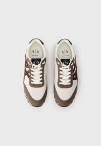 O pereche de adidași Armani Exchange alba și maro, cu detalii negre și portocalii ale logo-ului, văzuți dintr-o parte de sus pe un fundal alb.
