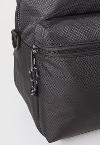 Angolo di una borsa di tessuto nero con texture, dotata di tasca con zip e tirazip a loop con dettaglio in corda bianca e nera.