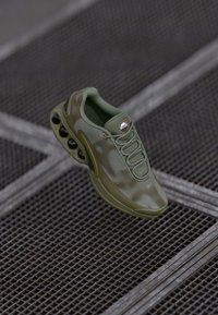 Green athletic shoe with a textured mesh upper, lacing system, and distinctive air cushioning pods along the sole.