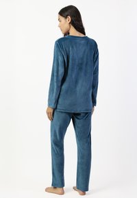 El conjunto de pijama azul de terciopelo incluye una camiseta de manga larga con cuello redondo y pantalones a juego, ambos suaves, lisos y sin adornos.