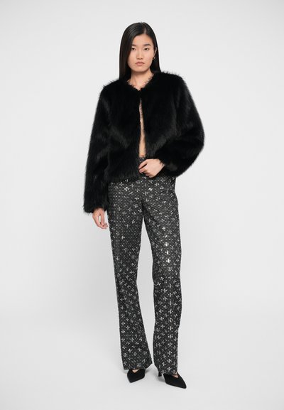 Zwarte faux fur jas met een ronde halslijn, gecombineerd met hoge zwarte broeken met zilveren pailletten sterpatronen. Zwarte puntige schoenen.