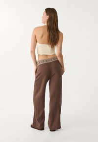 Bruna vida byxor med texturerat tyg och ett mönstrat midjeband, kombinerat med en krämfärgad stickad crop top. Enkel, avslappnad design.