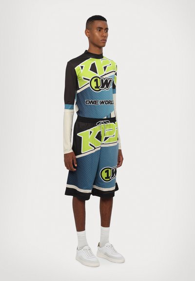 Farverigt basketball-outfit med en langærmet trøje i sort, grøn og blå med grafiske logoer, parret med matchende shorts.