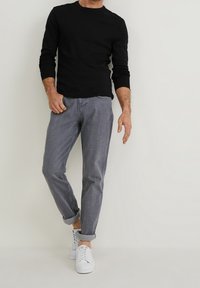 Camisa negra de manga larga, pantalones grises con puños y zapatillas blancas. La camisa tiene un escote redondo, y los pantalones tienen una textura sutil y un corte ajustado.