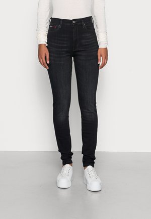Jeans ajustados de lavado oscuro con cintura alta, que presentan un diseño clásico de cinco bolsillos y detalles de costura sutiles, combinados con zapatillas blancas.