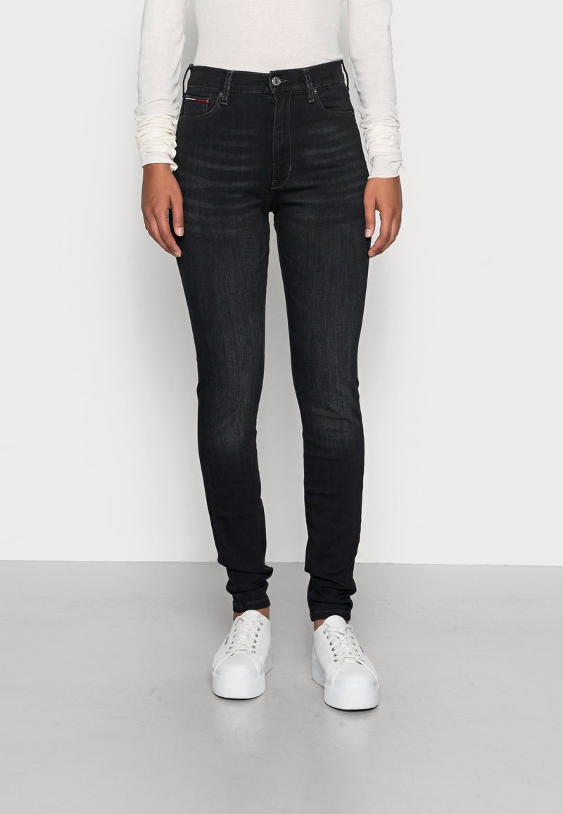 Jeans ajustados de lavado oscuro con cintura alta, que presentan un diseño clásico de cinco bolsillos y detalles de costura sutiles, combinados con zapatillas blancas.