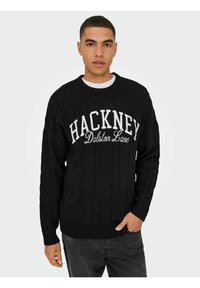 Schwarzer Kabelstrick-Pullover mit Rundhalsausschnitt und weißem Schriftzug "HACKNEY Dalston Lane" auf der Brust. Gerippte Bündchen und Saum.