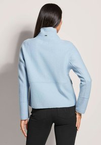 Light blue fleece jacket with a high collar and seam detailing, paired with black pants featuring a pocket design. Smooth texture overall.