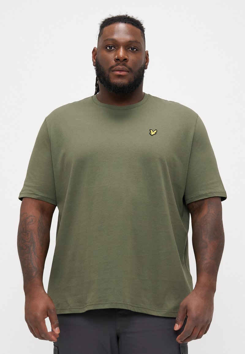Tricou scurt din bumbac moale, de culoare verde măslin, cu mânecă scurtă, guler rotund și un mic logo brodat galben pe piept. Croială obișnuită.