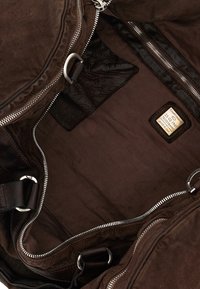 Interno di una borsa da viaggio in pelle marrone, caratterizzato da una texture liscia, zip in metallo e un'etichetta con testo impresso. Foderata con un tessuto scuro.