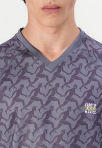 Športové tričko s výstrihom do V v sivej farbe s opakujúcim sa tmavosivým vzorom bežiacich postáv. Má malú logo v dolnom rohu.