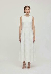 Robe blanche sans manches avec un motif œillet carré, design fluide et ourlet long. Portée avec des sandales blanches à lanières.