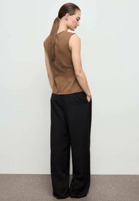 Bruine mouwloze top met een gestructureerde pasvorm, gecombineerd met zwarte wijde broek. Gladde textuur en minimalistisch ontwerp zonder zichtbare patronen.