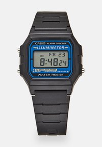 Montre numérique avec bracelet en caoutchouc noir, cadran rectangulaire, accent bleu autour d'un affichage gris. Les caractéristiques incluent une alarme et une résistance à l'eau.