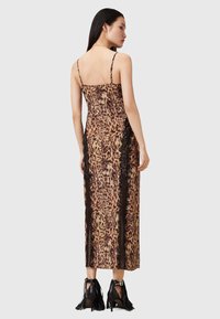 Abito di media lunghezza con stampa leopardata e dettagli in pizzo, caratterizzato da spalline sottili e una silhouette aderente. Scarpe con tacco alte decorate con nappine nere.