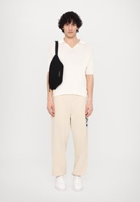Off-white rebrovaný polo s krátkym rukávom, béžové široké nohavice, čierna crossbody taška, biele tenisky; elegantný, moderný dizajn s hladkými textúrami.