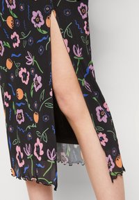 Svart blommig klänning med en sidoklyvning. Har ett mönster av färgglada blommor och blad, texturerad tyg och en scalloped nederkant.