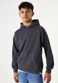 Sudadera gris oscuro hecha de tejido suave, con un bolsillo frontal, capucha con cordón y puños acanalados. Ajuste casual con una etiqueta en el dobladillo.