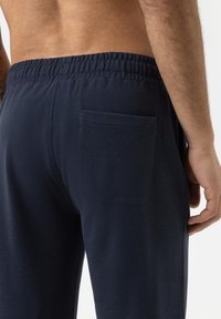 Marineblauwe joggingbroek van zachte stof, met een elastische tailleband en een achterzak aan de rechterkant. Gladde textuur zonder patronen.
