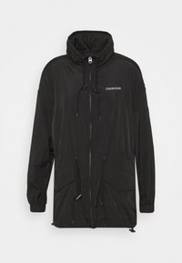 Svart lättviktsjacka med hög krage, dragsko i midjan, dragkedjestängning och sidofickor. Har Calvin Klein-logotypen i vitt.