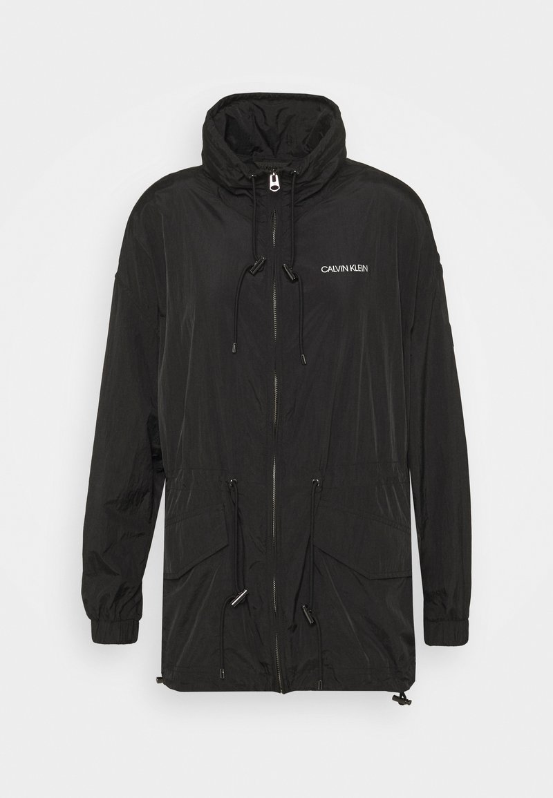 Black lightweight jacket with a high collar, drawstring waistband, zip closure, and side pockets. Features Calvin Klein logo in white.