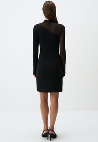 Zwarte jurk met lange mouwen; doorschijnend bovenrugdeel; getailleerd ontwerp; zachte textuur; knielang; minimalistische stijl zonder aanvullende patronen.