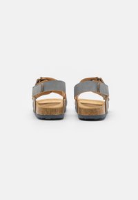 Grå sandaler med bruna läderaccenter, justerbara remmar och ett korkfotbett; texturerad sula för grepp; öppen bakdesign.