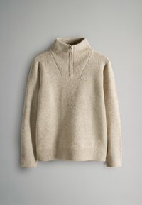 Jasno beżowy sweter z wysokim zamkiem, posiadający teksturowany wzór dzianiny, ściągacze na mankietach oraz luźny krój. Miękka tkanina.